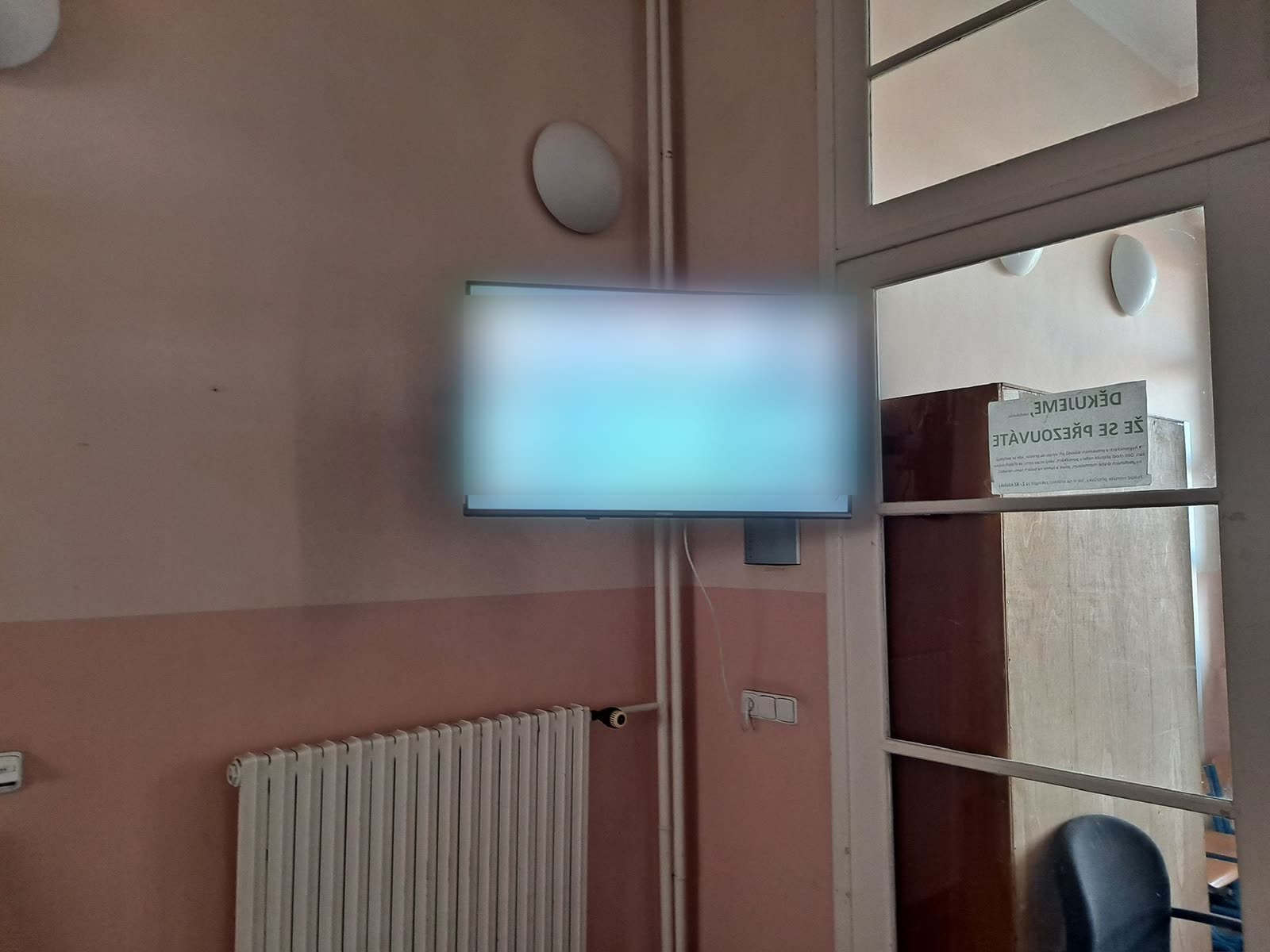 Obrazovka se světlým motivem suplování na zdi vedle prosklených dveří