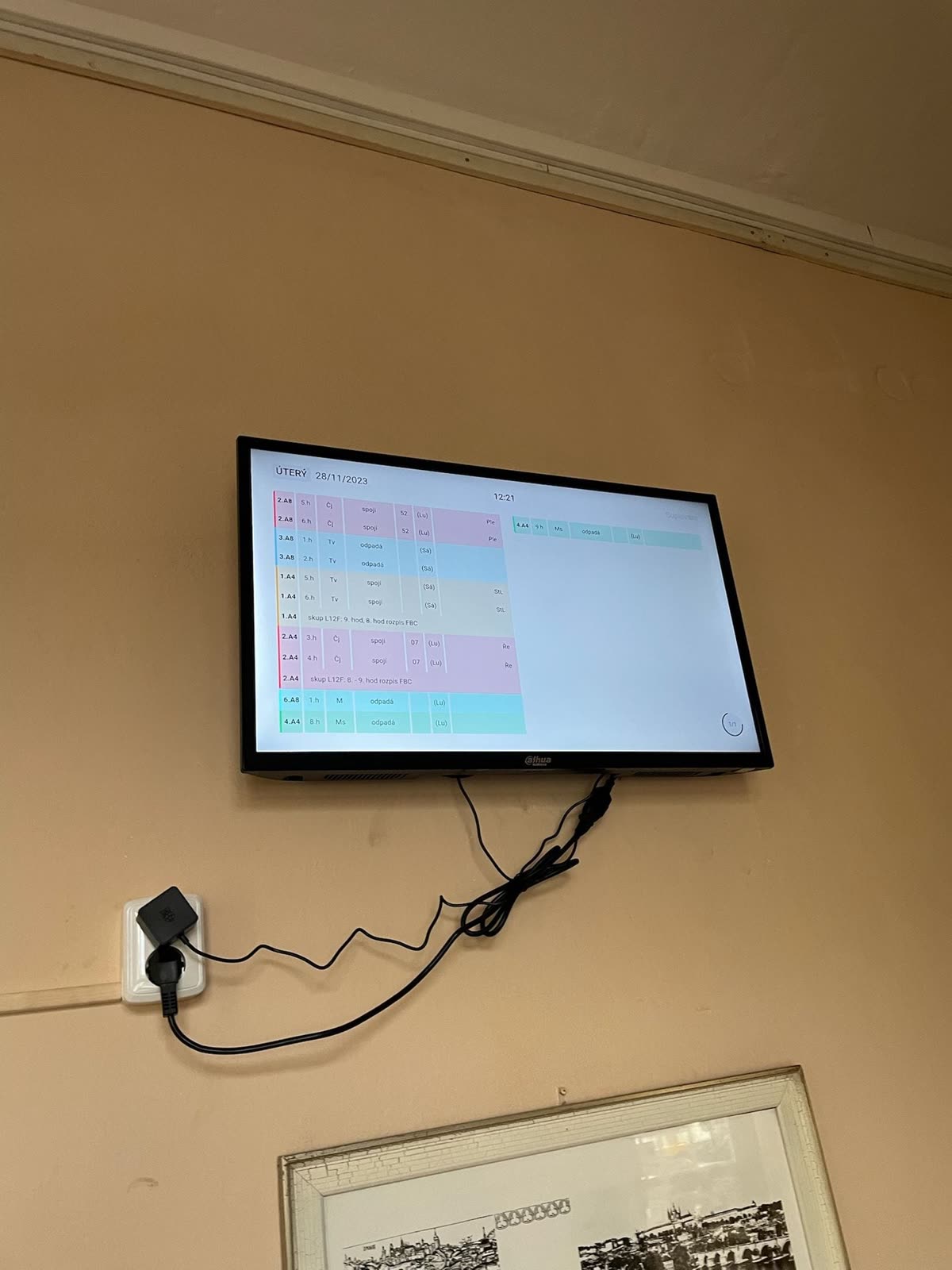 Obrazovka se suplováním ve světlém motivu, kabel vede k zásuvce přímo pod ní