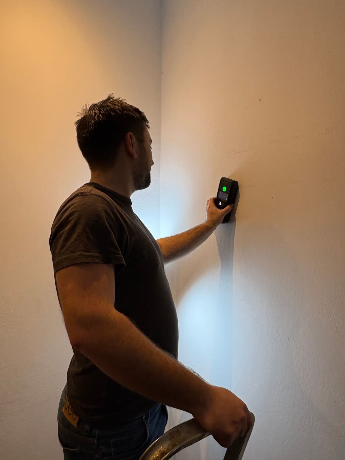 Technician placing a detector on the wall to find wiring before drilling