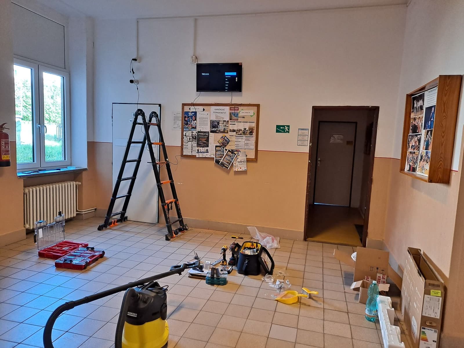 Montáž na chodbě: po nás zůstane jen hotová obrazovka, vysavač jde s námi Rozdělaná instalace na školní chodbě: žebřík, nářadí a vysavač, na zdi už visí nová televize