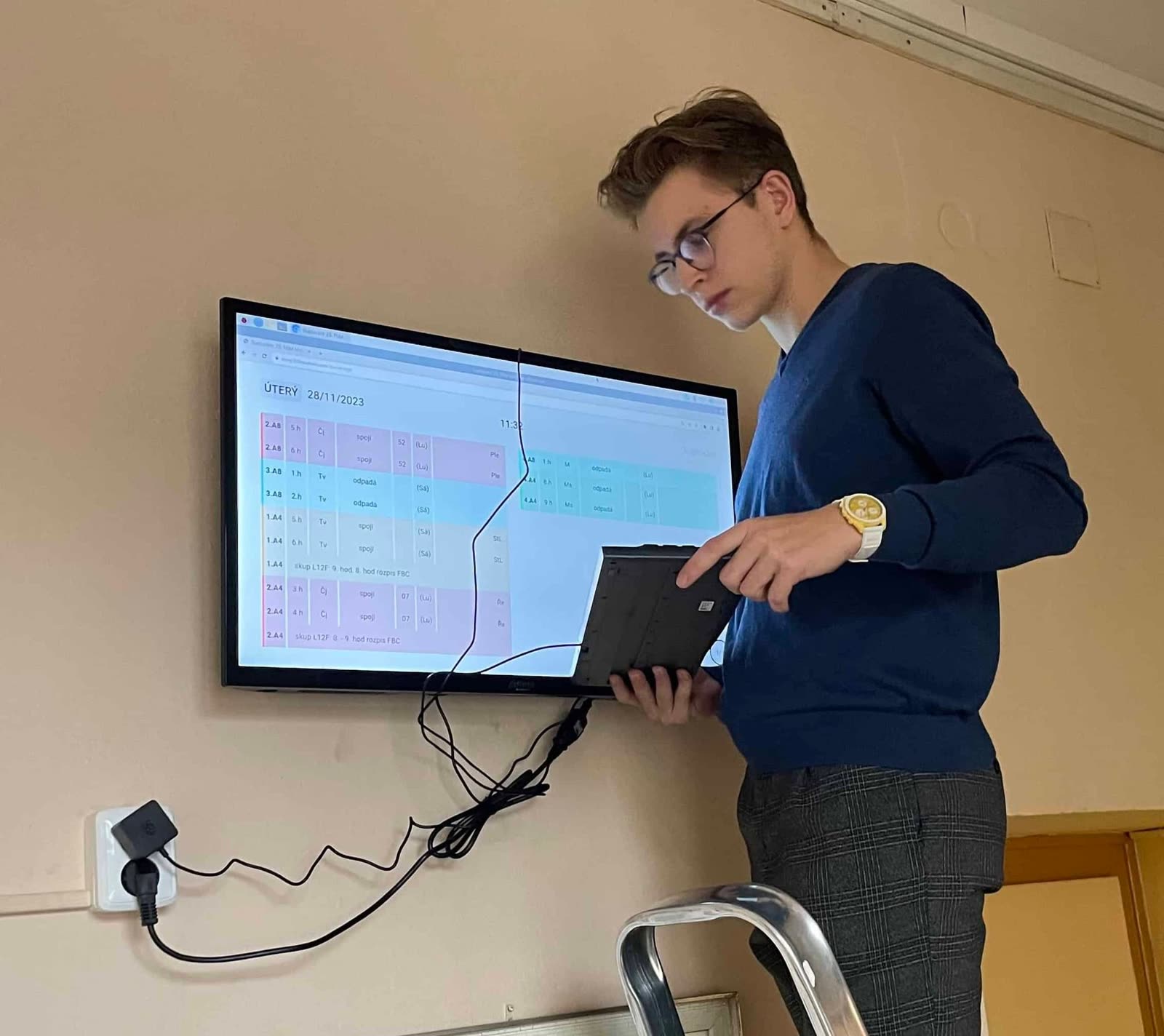 Technician with a laptop setting up the newly hung screen with substitution schedule