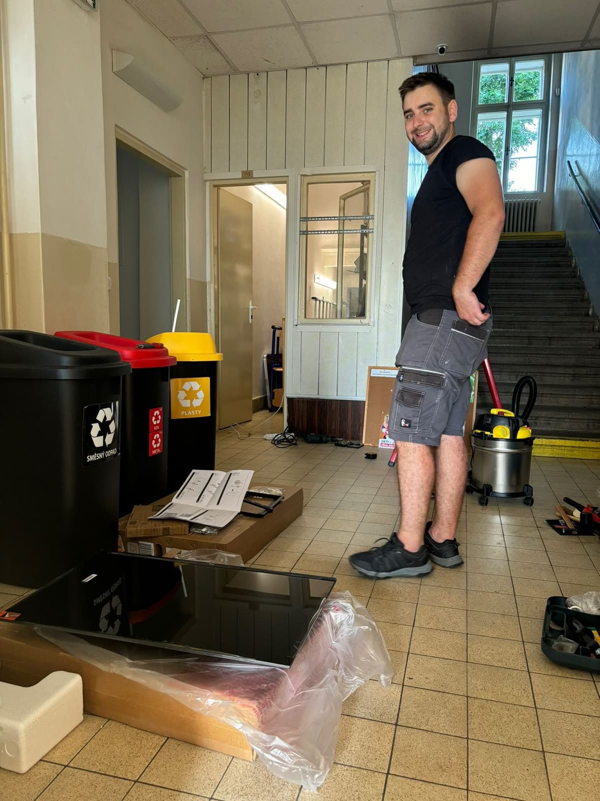 Technician in the entrance hall among the TV box, vacuum cleaner, and recycling bins