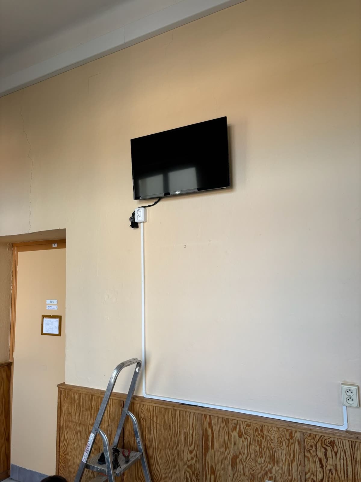 Nově pověšená televize na zdi, kabel vede v bílé liště dolů k zásuvce